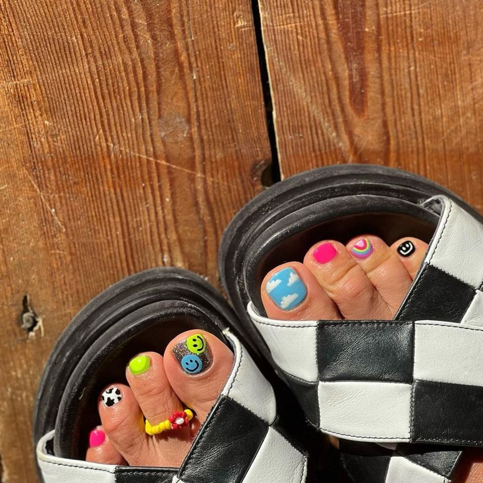 Colorful neon mismatch pedi with cow print, smiley faces, clouds, and rainbows - InStyle Spring Pedicure Ideas