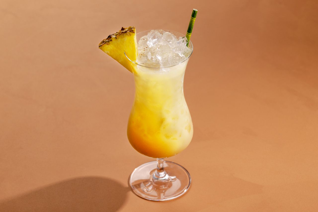 A painkiller cocktail with a paper bamboo straw on a peach background.