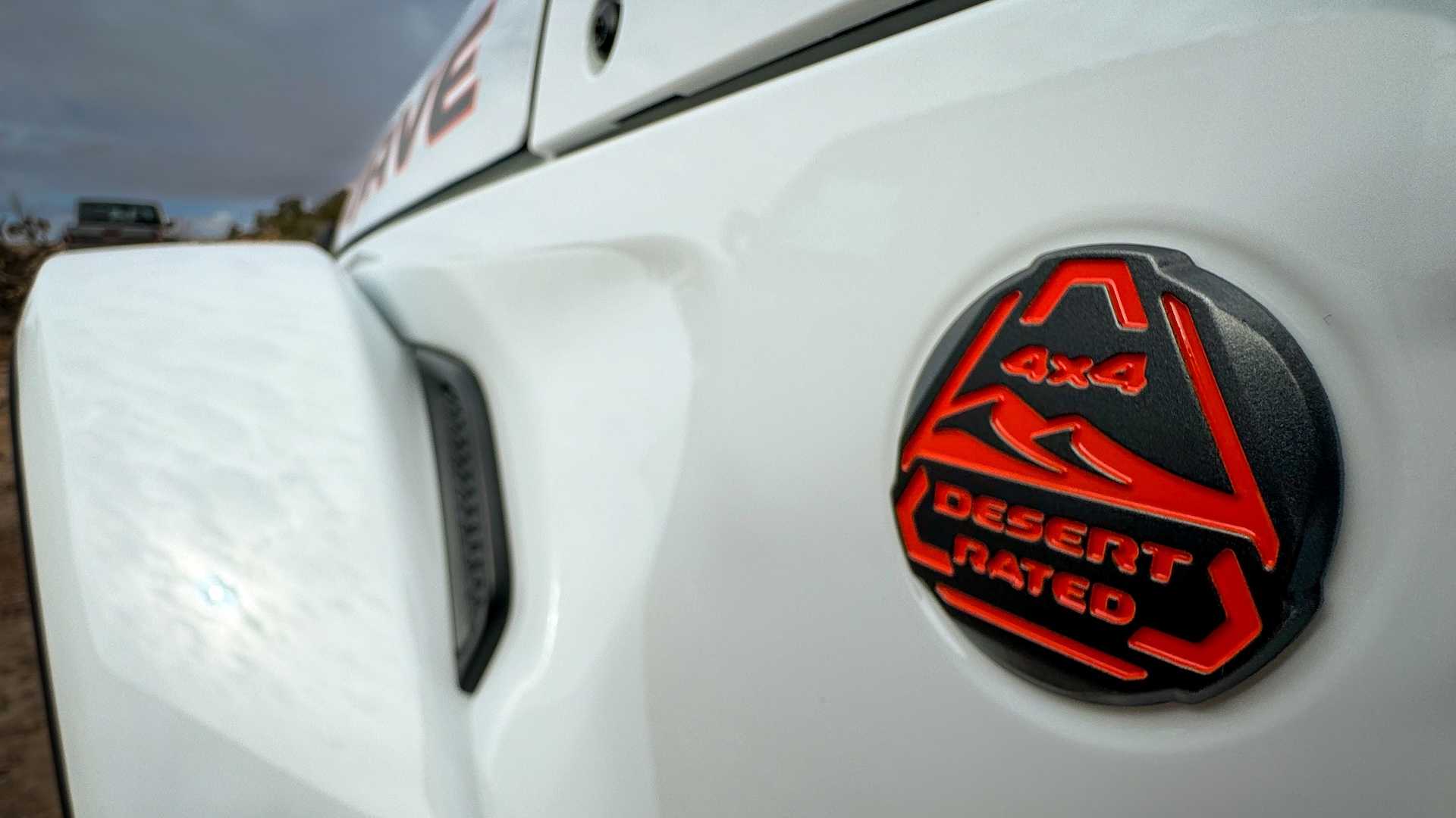 Desert trail rated badge on the fender of a white pickup truck, the desert visible in the background.