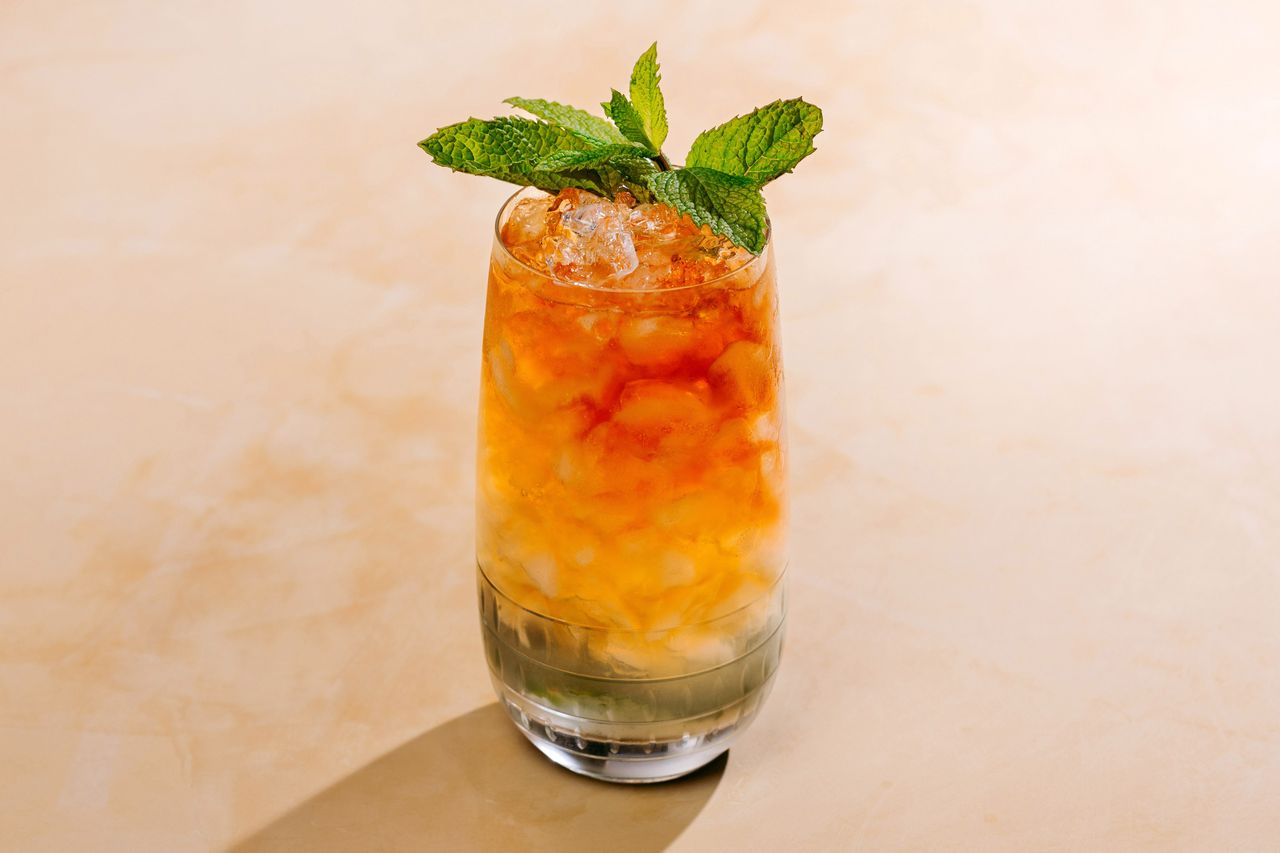 A Queen's Park Swizzle cocktail on a peach colored surface.
