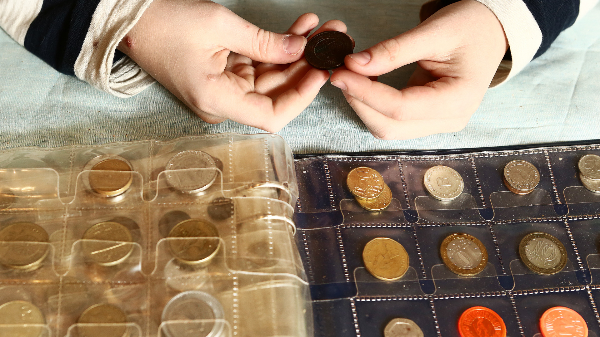 Discover a person holding a coin with an album full of a variety of collectible coins sitting on a table