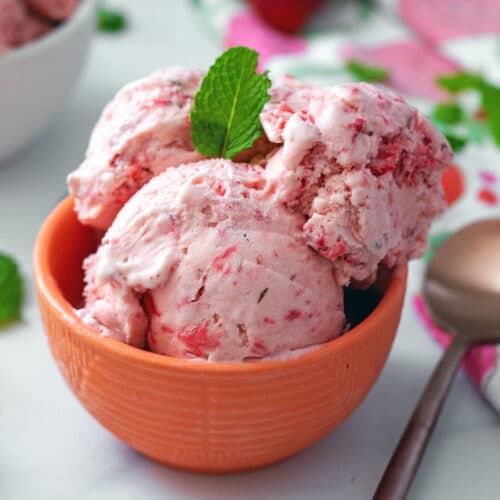 Head-on closeup view of strawberry mint ice cream in a bowl with a rose gold spoon on the side