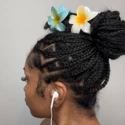 Person with braided hair styled in a bun, adorned with two floral hair clips, and wearing earbuds