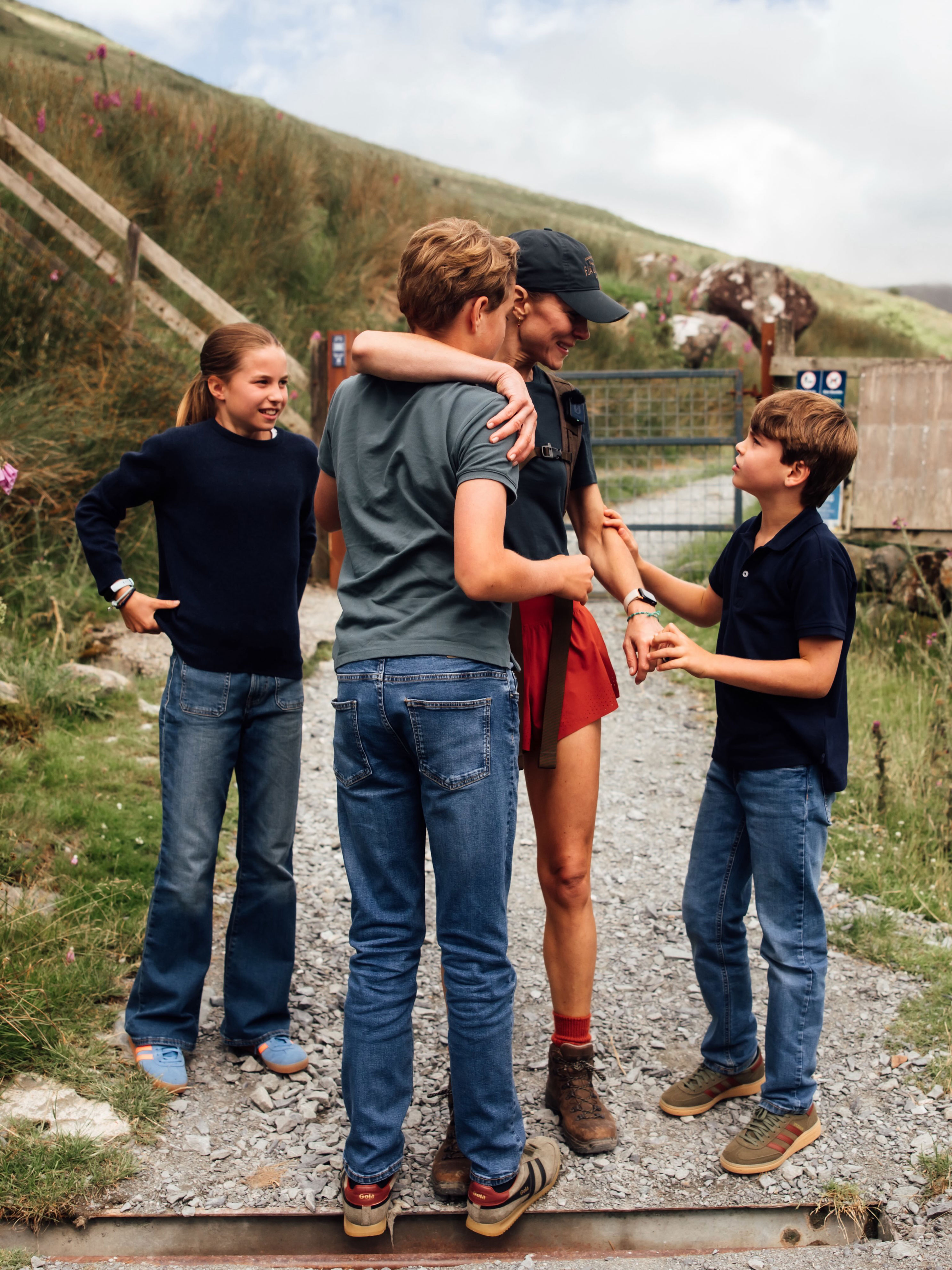 Princess Kate, wore is wearing red shorts and navy baseball cap, is greeted by her three children, Princess Charlotte, Prince George, and Prince Louis, who all wear matching denim jeans