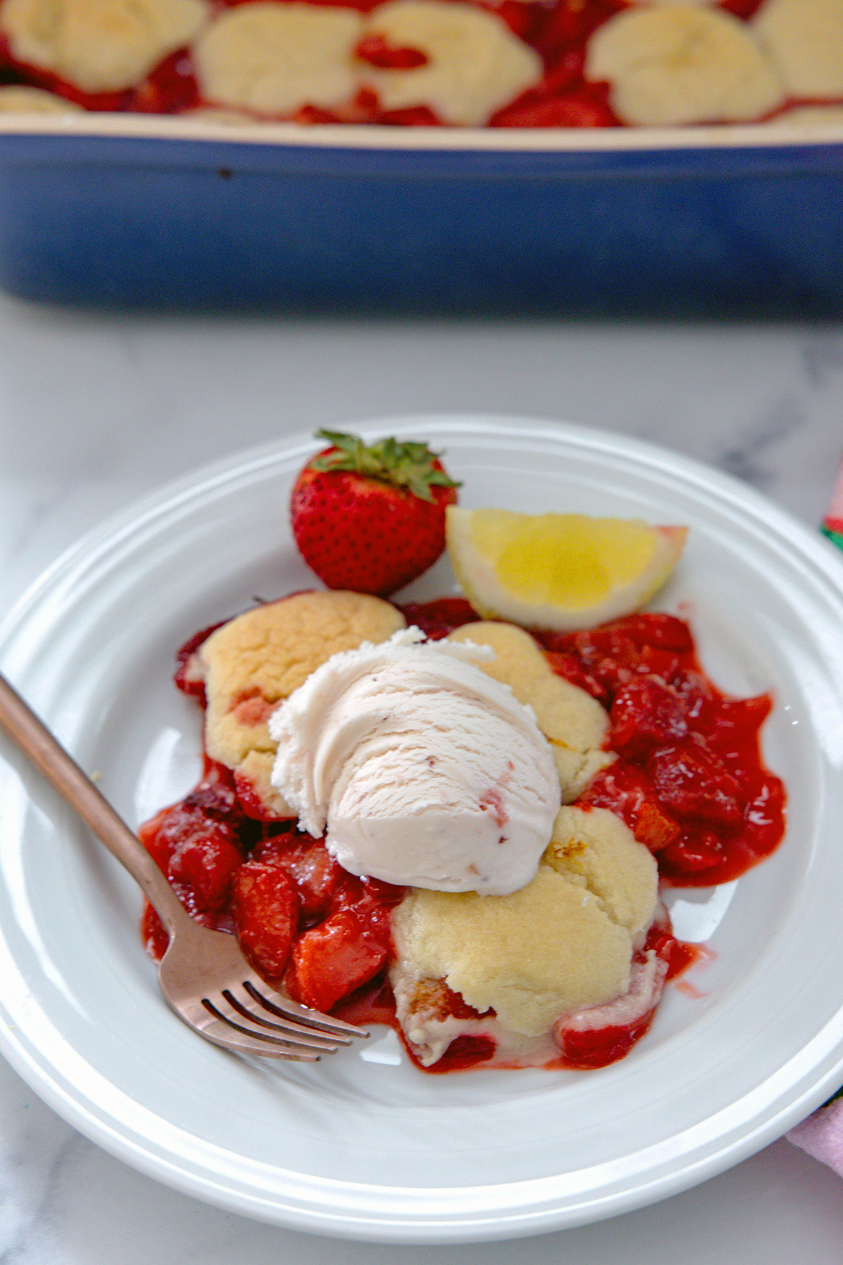 Strawberry lemonade cobbler on a plate topped with strawberry ice cream with recipe title at top of photo.