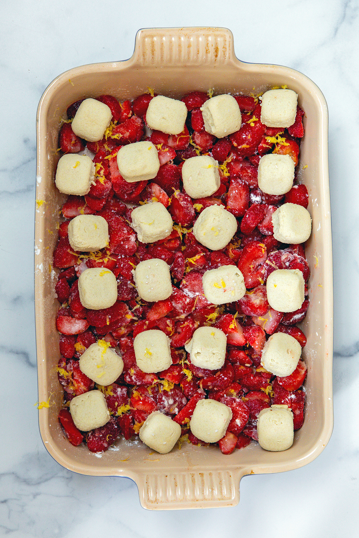 Strawberries and lemon in baking dish and topped with cookie dough pieces.