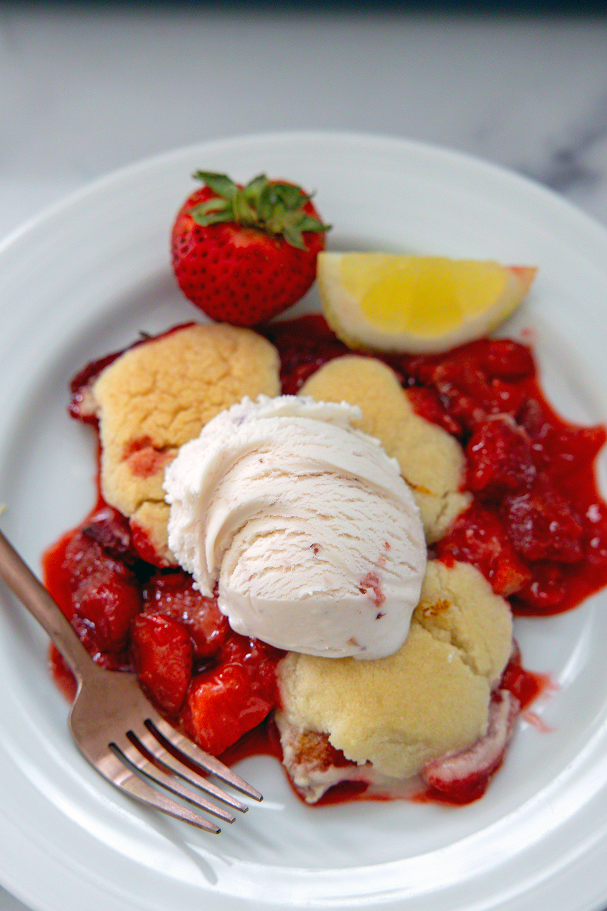 Closeup view of a strawberry cookie cobbler with scoop of strawberry ice cream and a fork.