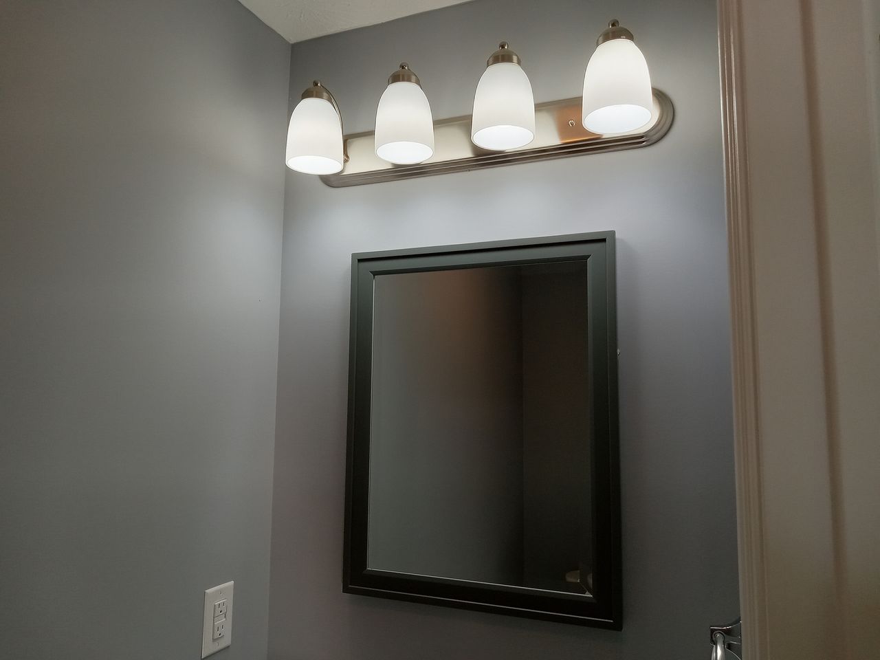 A bathroom wall with a mirror light fixture and gray paint