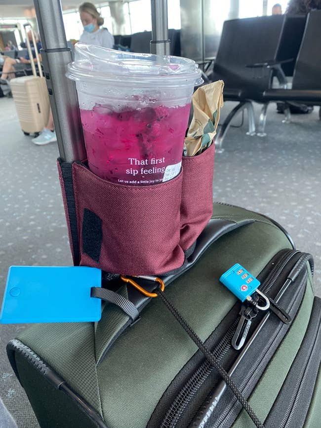 A drink caddy attached to a suitcase handle holding a starbucks cup and sandwich