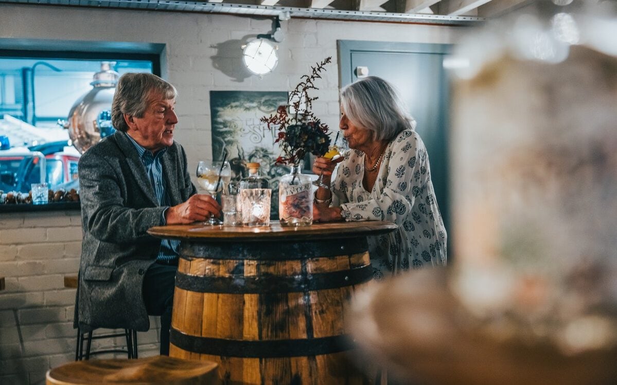 A man and a woman sipping drinks at a high-top table made from a barrel