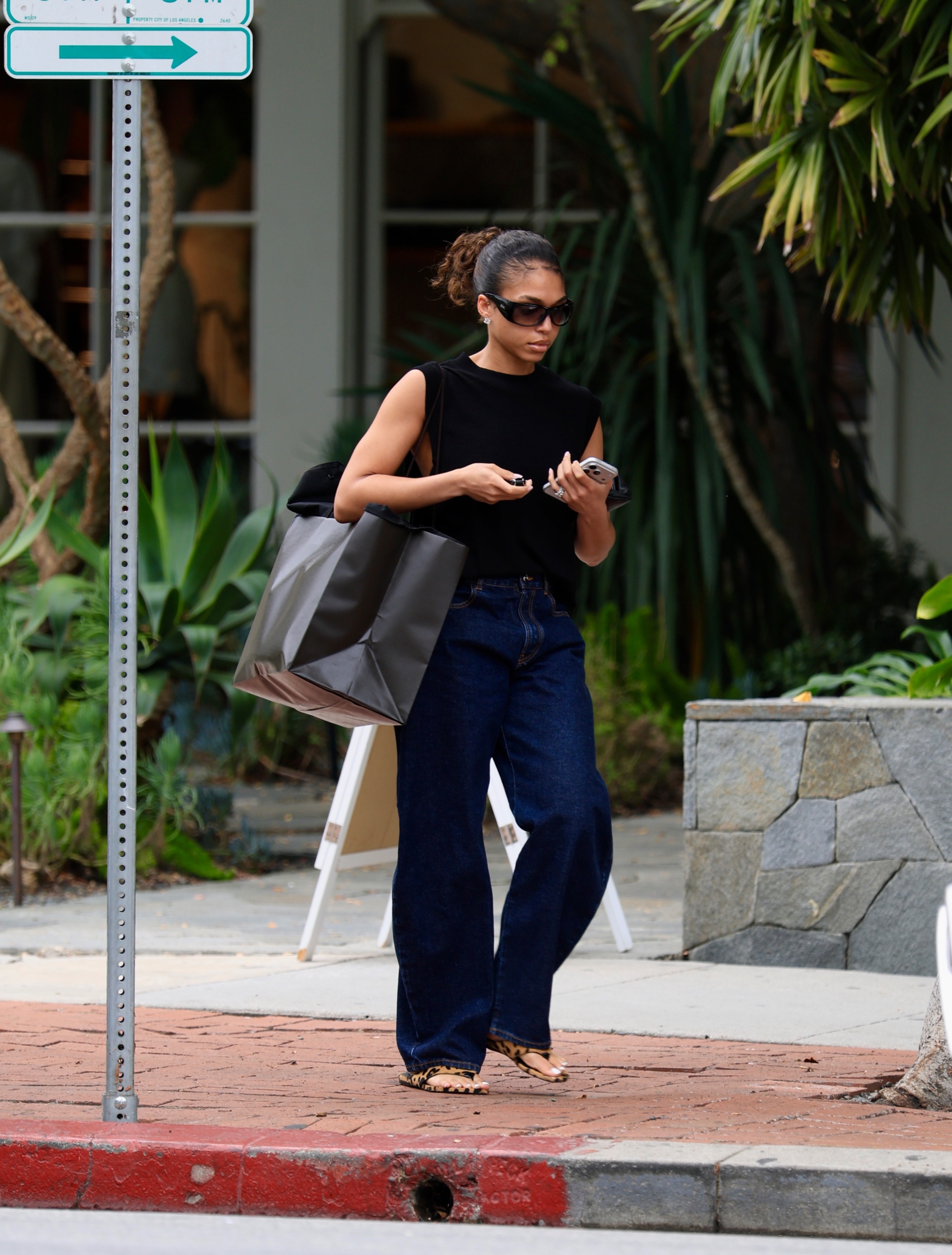 Lori harvey wears a black tank top, dark-wash jeans, leopard-print flip-flops and sunglasses.