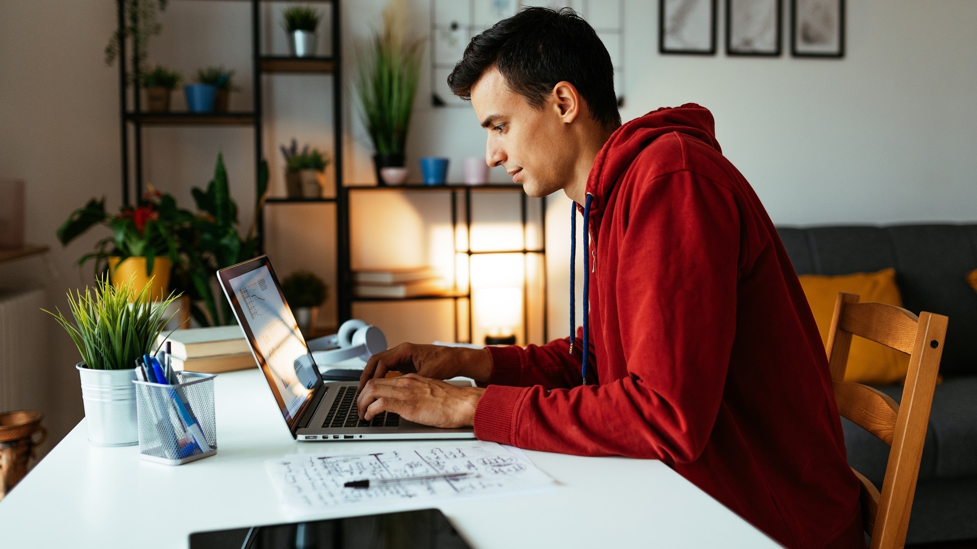 Discover a young man working on his computer at home, doing remote work or online side hustle.