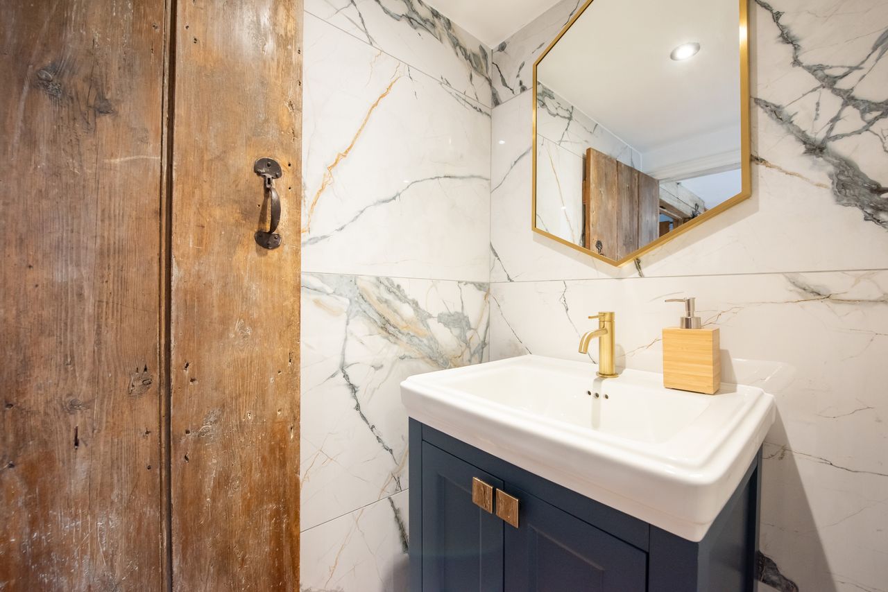 A bathroom sink area with a wooden door and a hexagonal mirror mounted on a marble wall