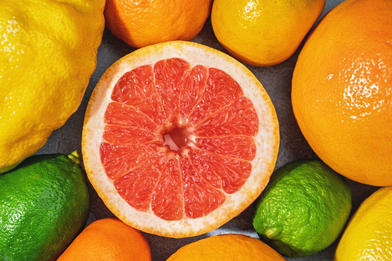 A variety of citrus fruits including a cut grapefruit lemons limes oranges and mandarins arranged together