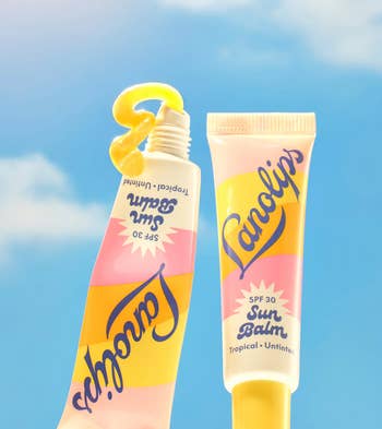 Two tubes of Lanolips SPF 30 Sun Balm, one with balm coming out. Background shows a clear sky