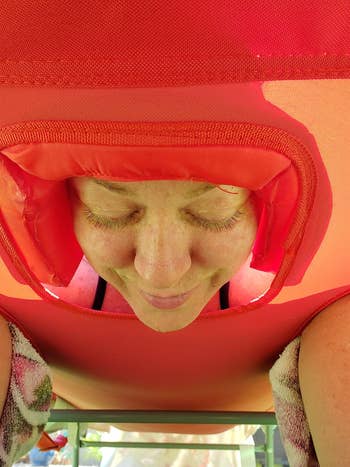 Reviewer laying on their stomach on the red chaise lounge with their face in the hole