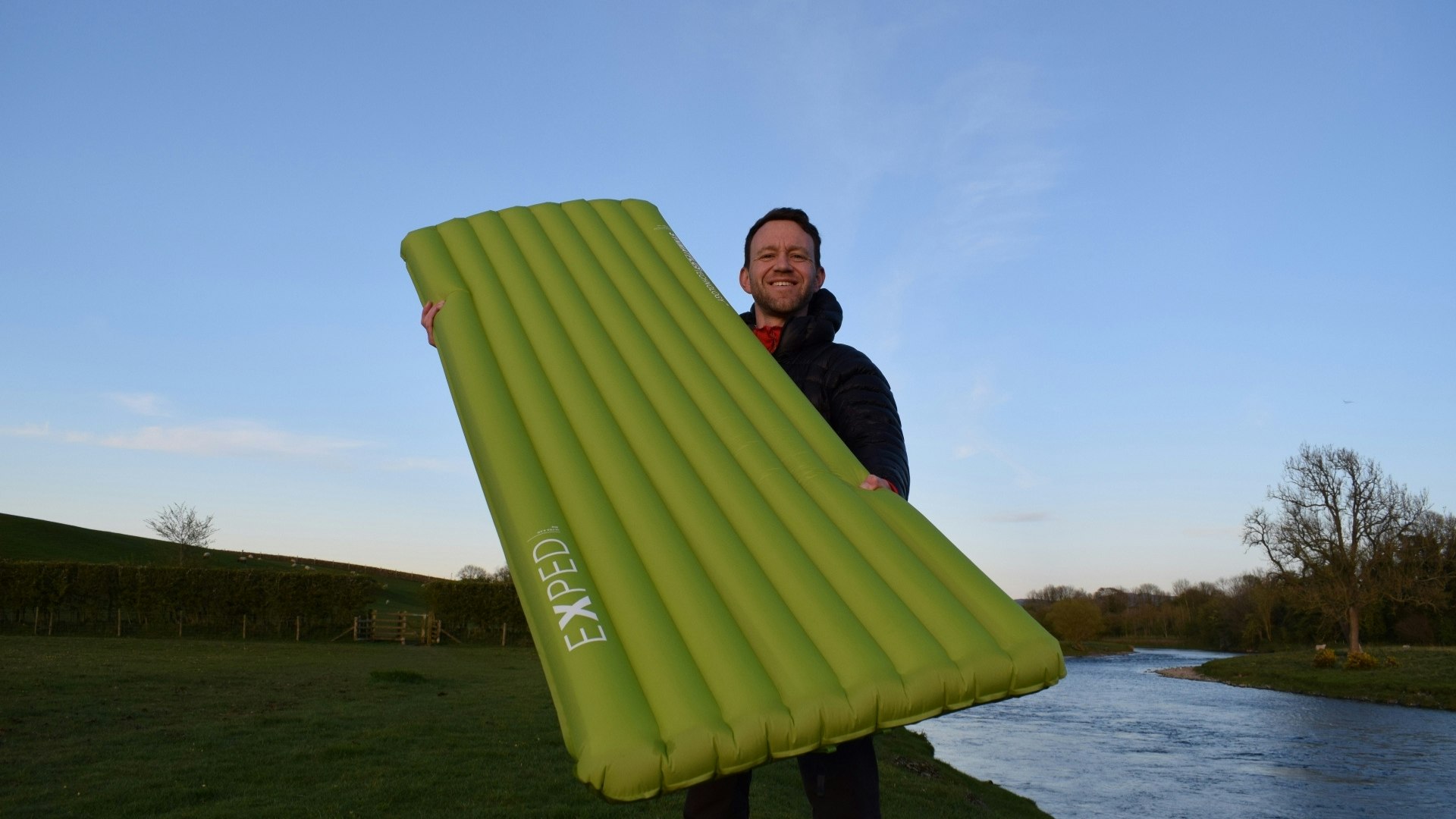 James holding the inflated Exped Ultra 6.5R sleeping mat outdoor by river