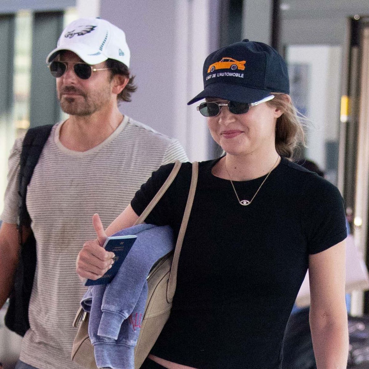 Gigi Hadid wearing a black T-shirt with cropped cargo pants and flip-flops at the airport with Bradley Cooper