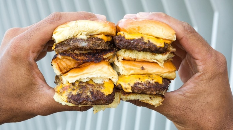 Both hands holding four Chili's Big Mouth Bites , mini burgers with cheese, with a neutral background.