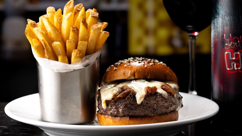 Capital Grille cheeseburger on a plate next to a side of French fries wrapped in paper in a metal serving container and wine.