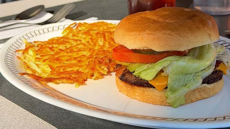 Waffle House cheeseburger dressed with lettuce, tomato and pickles on a diner plate with hashbrowns.