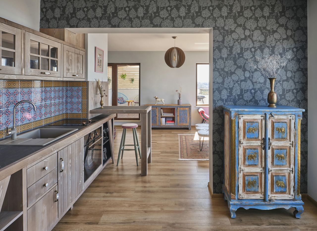 A view of a kitchen and adjoining living area with wooden flooring and cabinets with a colorful blue cabinet on the right