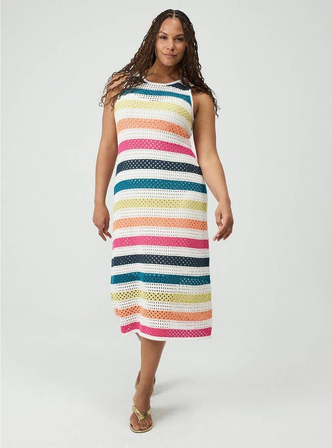 Model wearing a sleeveless, knee-length crochet dress with horizontal white and colorfulstripes