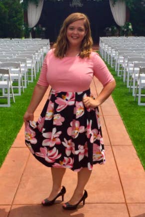 A reviewer wearing the knee-length dress with a pink bodice and black and pink floral skirt