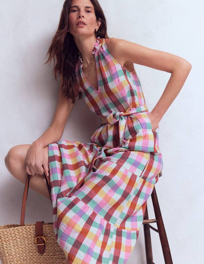 model in sleeveless white and colorful pastel checked midi with ruffle at collar of v-neckline and matching tie belt, with hand in pocket