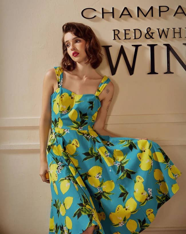 Person in a lemon-print summer dress poses against a wall with beverage words, possibly in a stylish shopping context