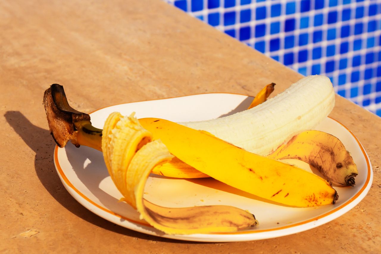 A partially peeled banana on a plate by a poolside