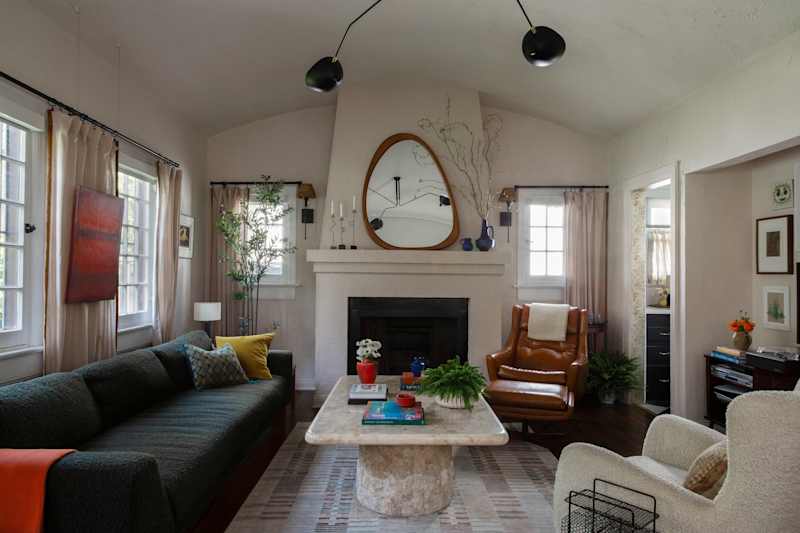 Cozy living room featuring a dark green sofa, a marble coffee table, and a leather armchair, with plants and artwork