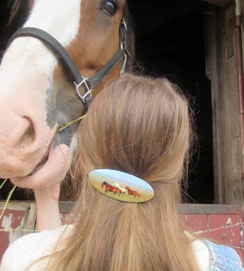 Woman with horse-themed hair accessory pets a horse in a stable