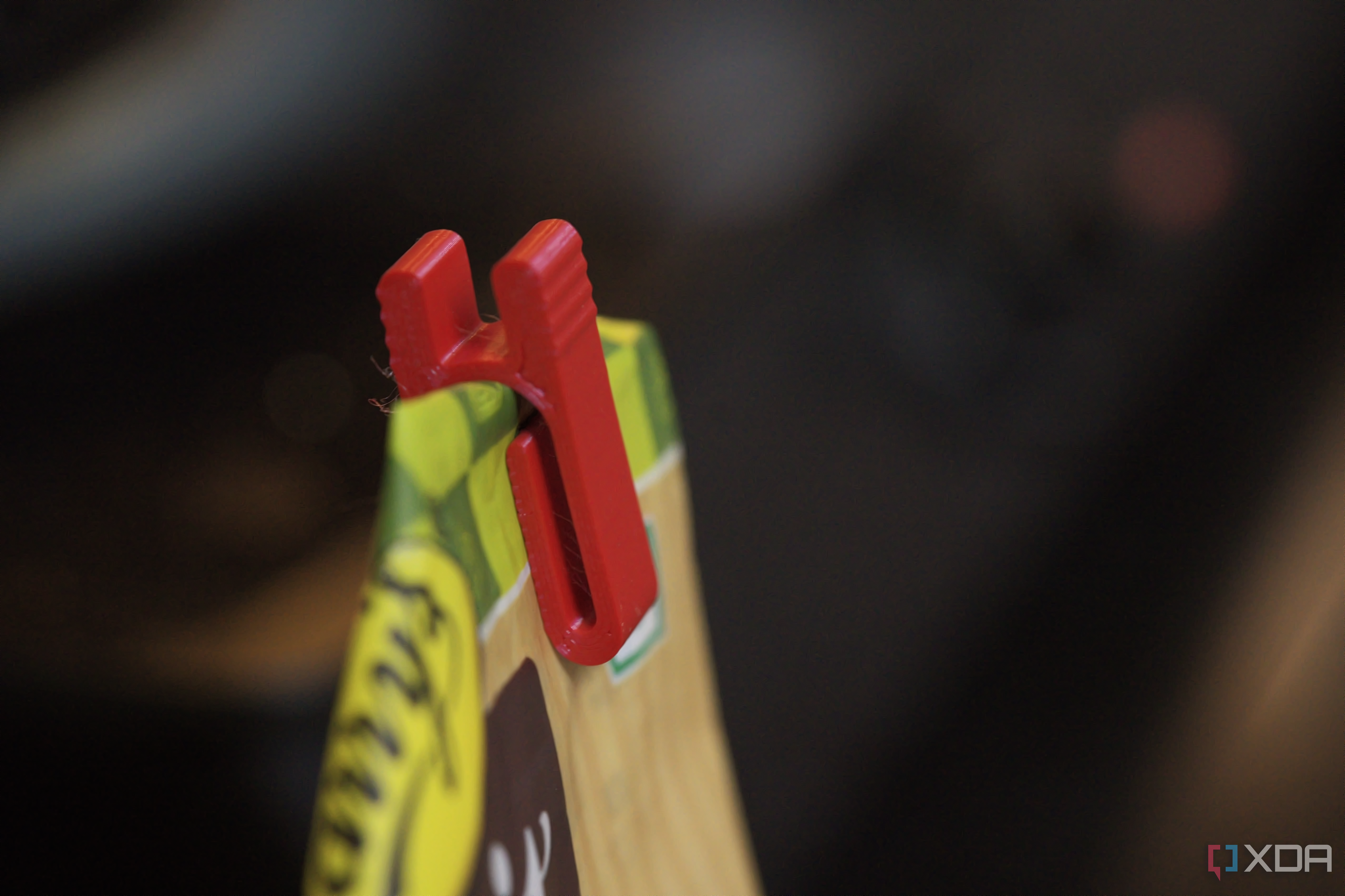 Side angle of a red bag clip on a brown bag against a blurry black background