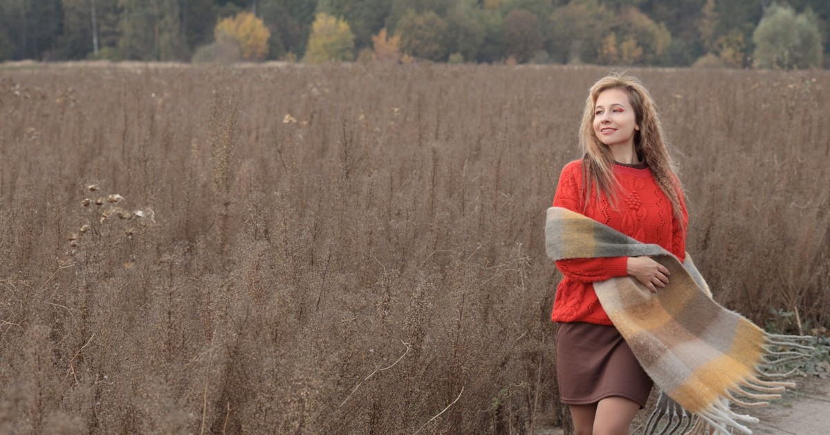 A woman in a red sweater and scarf walking through an autumn landscape, enjoying a peaceful moment.