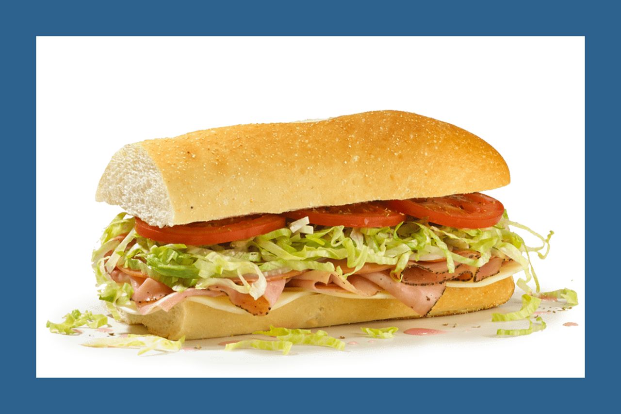 A submarine sandwich with deli meats shredded lettuce and tomato slices on a baguette