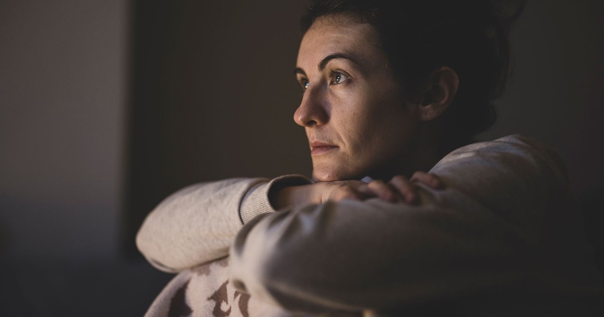 A woman sits in a dimly lit room, lost in thought, capturing a serene moment.