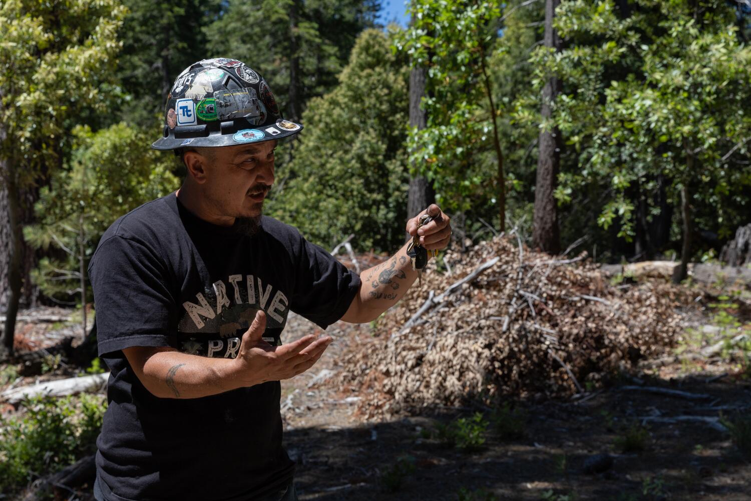 Matthew Williford Sr., wearing a hard hat, gestures while speaking near a burn pile