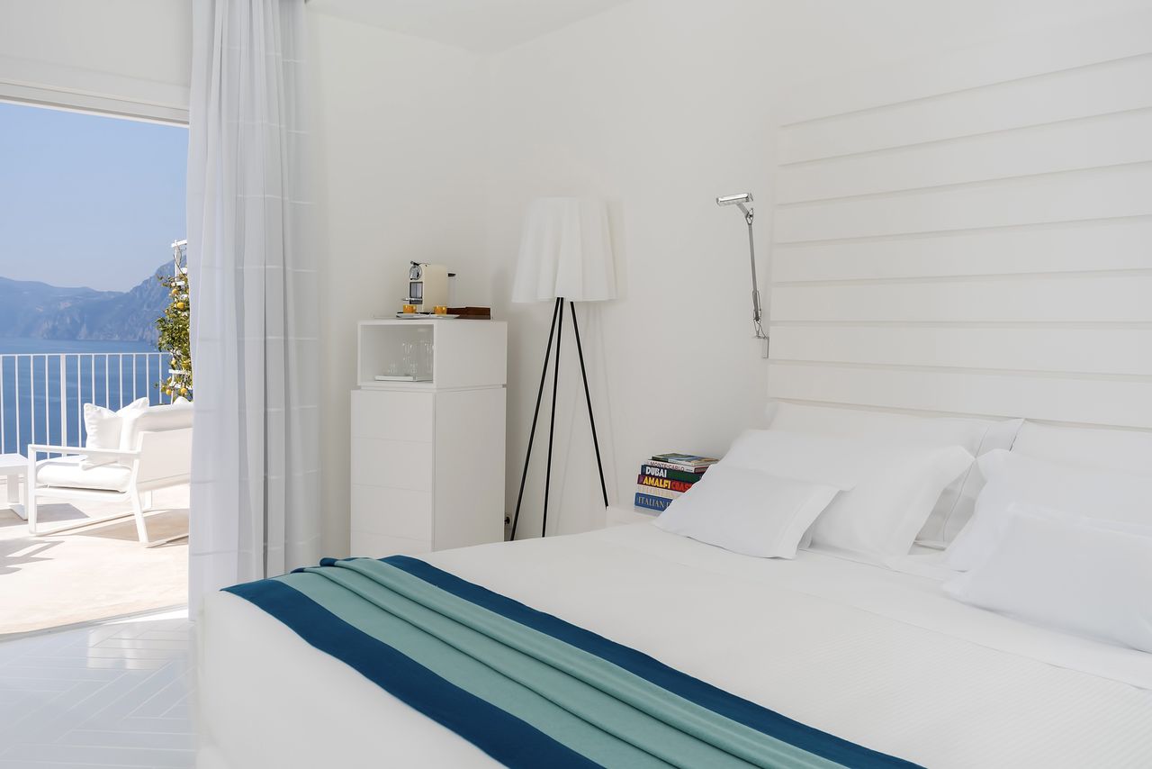 A hotel room with a bed a small refrigerator a lamp and an ocean view through an open sliding door
