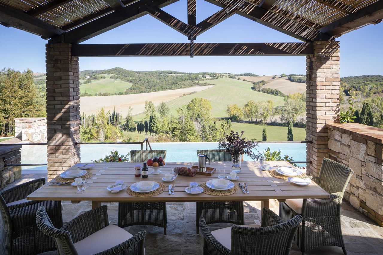 Outdoor dining table under a pergola with a scenic view of the countryside