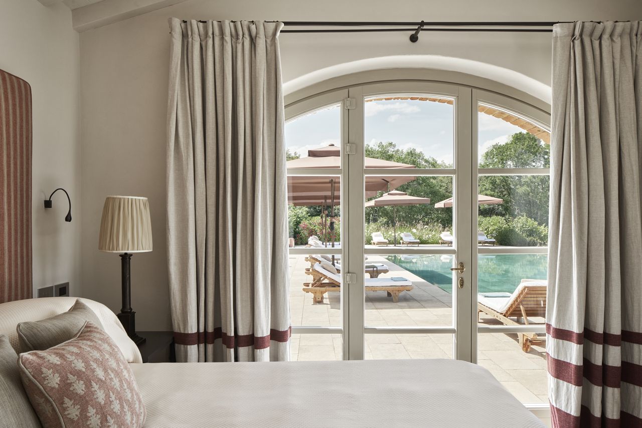A luxurious villa bedroom with a view through doors revealing a pool and outdoor seating