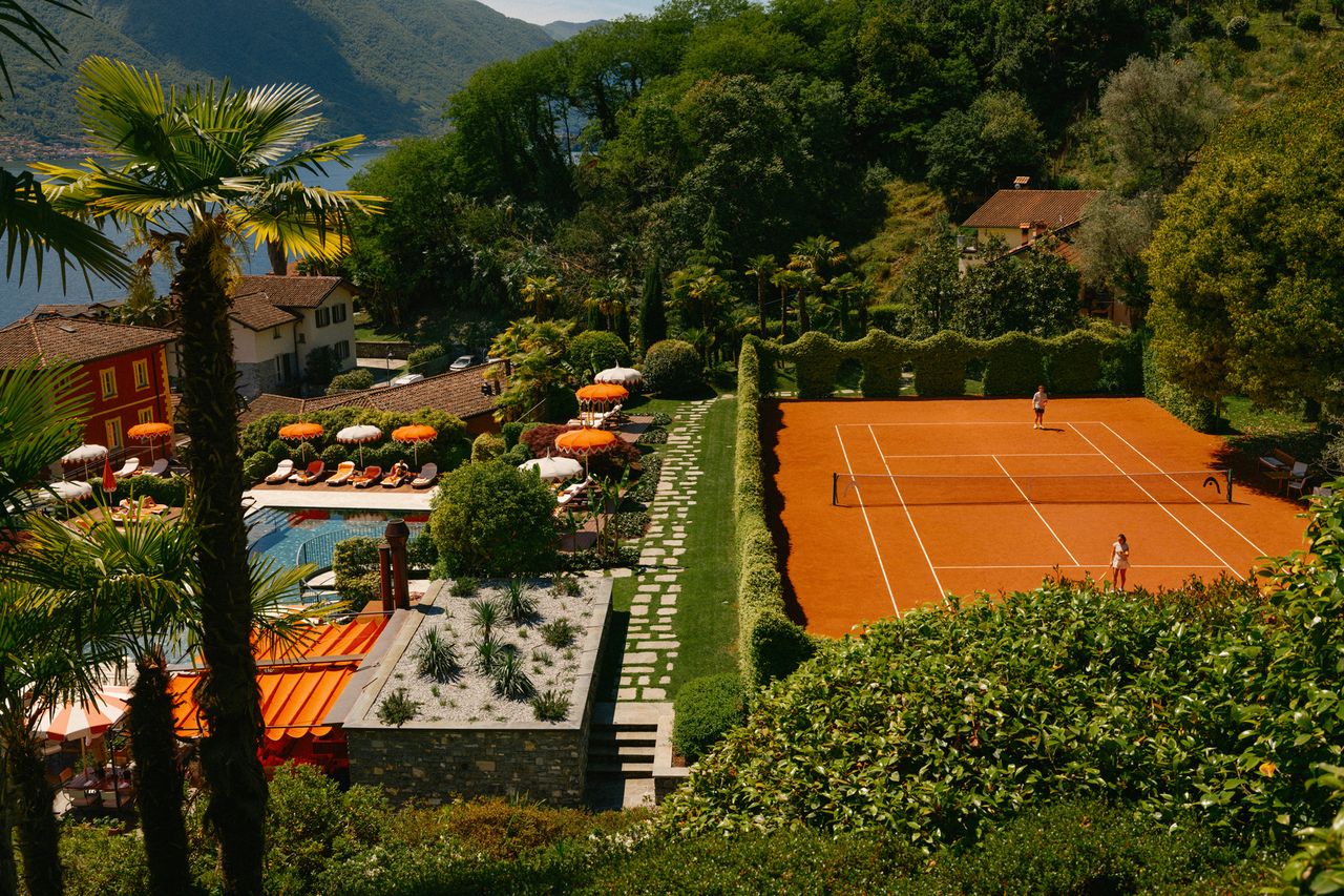 A tennis court near a pool with sun loungers surrounded by lush greenery