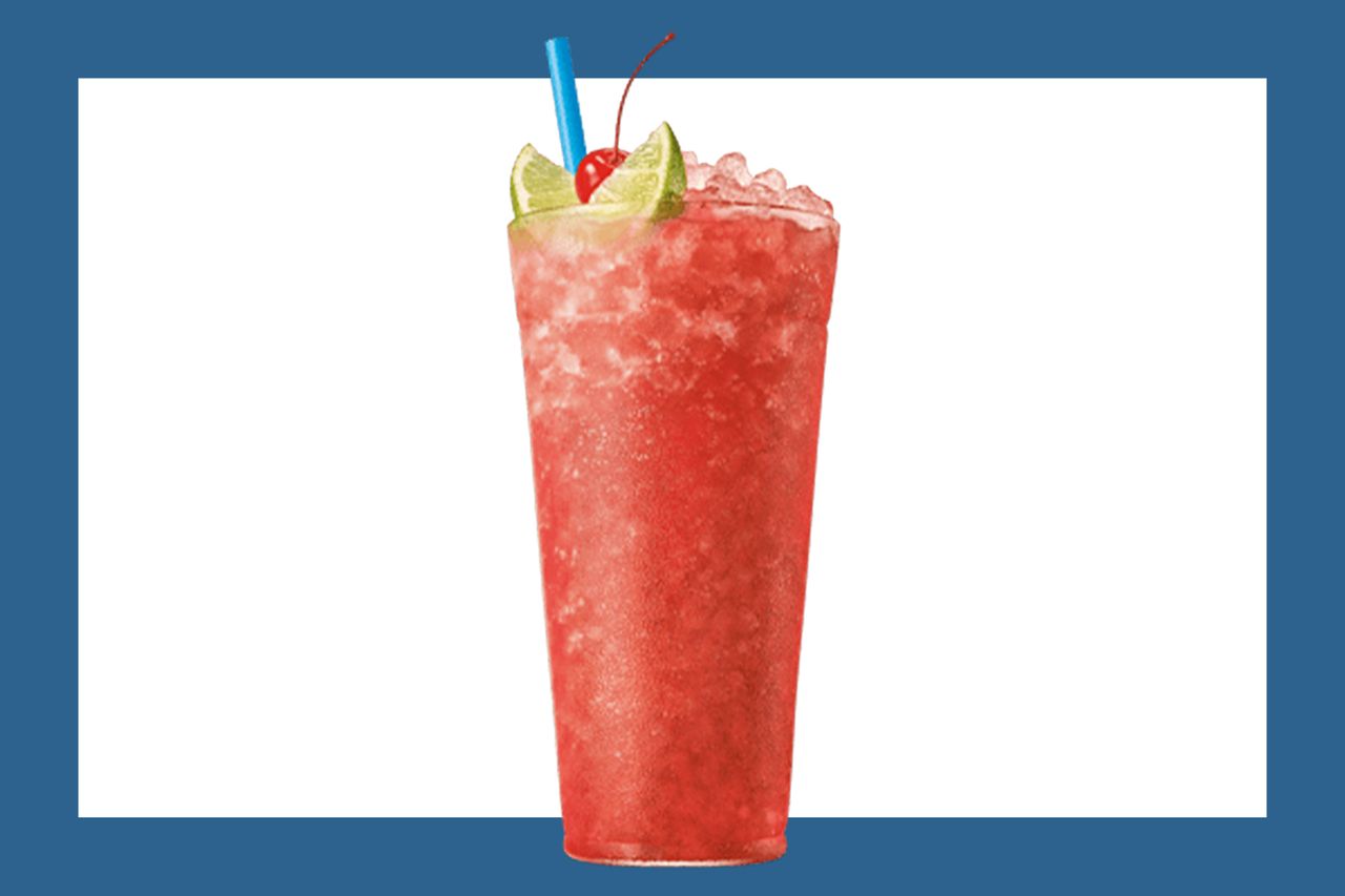 A slush drink with lime wedges a cherry on top and a straw