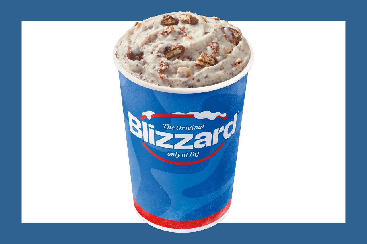 A Dairy Queen Blizzard dessert in a branded cup topped with bits of nuts or candy displayed against a blue background