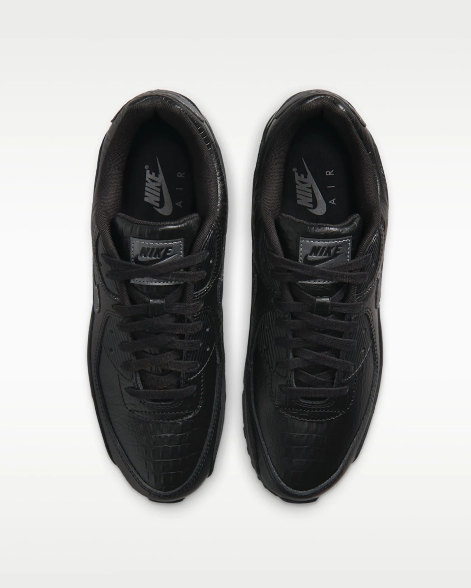 Pair of black Nike Air sneakers with textured leather and black laces viewed from above.