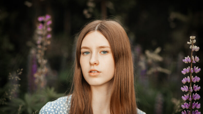 A young beautiful girl with long red hair in a clearing among the flowers. Lupines