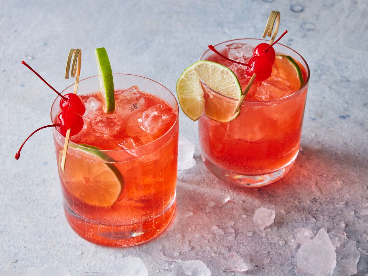 Two cherry bomb drinks, garnished with slices of lime and maraschino cherries