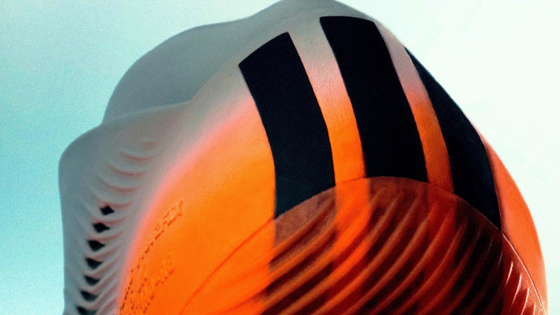Close-up of an orange and white soccer cleat with black stripes on the sole.