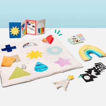 Baby sensory play mat with various textured shapes, a dangling star toy, and a colorful book. Includes high-contrast cards and a rainbow pillow
