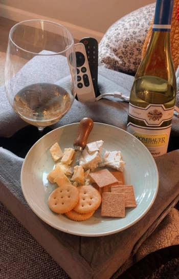 Plate of assorted cheeses and crackers with a glass of white wine on a tray, remote control in the background